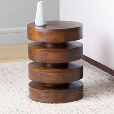 a wooden table with a white vase sitting on it's top next to a rug