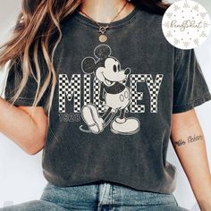 a woman wearing a mickey mouse t - shirt with her hands in her pockets and the words mickey on it