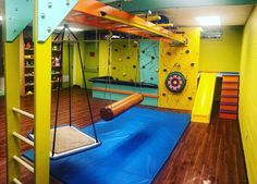 an indoor gym with swings, climbing walls and wooden flooring in the middle of it