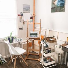 an artist's studio with easel, canvass and paintings on the wall