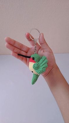 a hand holding a small crocheted keychain with a bird on it