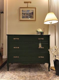 a green dresser sitting next to a lamp on top of a wooden table in a living room