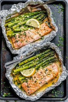 salmon and asparagus wrapped in foil with lemon wedges on top, ready to be served