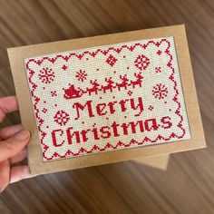 someone holding up a cross stitch christmas card