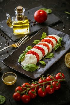 sliced mozzarella with tomatoes and basil on a plate next to olive oil, lemon wedges and cherry tomatoes