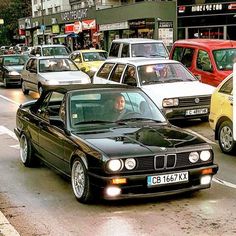 a black car driving down a street next to tall buildings and parked cars on the side of the road