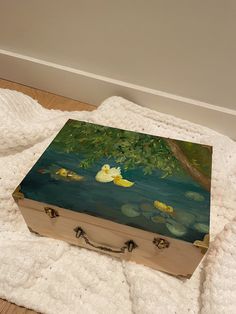 a wooden box sitting on top of a white blanket next to a tree and water