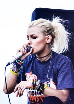 a woman with blonde hair and piercings on her fingers is singing into a microphone