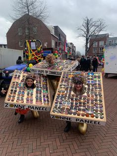 two people sitting on top of tables made out of cupcakes with faces painted on them