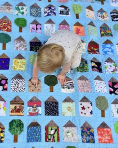 a young child is playing on a quilt made with houses and trees in various colors