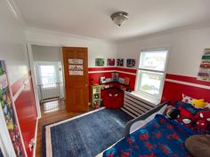 a bedroom with red walls and spiderman bedding in the corner, along with two windows