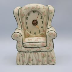 a white clock sitting on top of a chair with floral fabric around the armrests