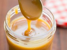 a spoon full of caramel sauce being poured into a mason jar with a wooden spoon