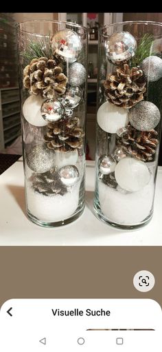 two glass vases filled with snow and pine cones