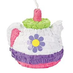 a teapot shaped ornament with a flower on the front and purple, green, pink, and white ruffled bottom