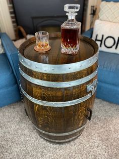 two glasses sitting on top of a barrel next to a bottle of whiskey in front of a couch