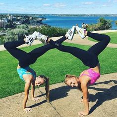 two women doing handstand exercises in front of the ocean and cityscape