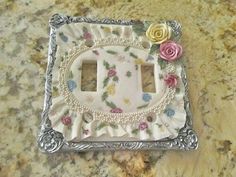 a decorative light switch cover with flowers and pearls in the center on a marble countertop