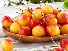 a wooden bowl filled with lots of red and yellow cherries on top of a table