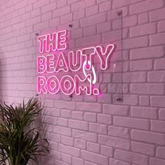 a pink neon sign that says the beauty room on a brick wall next to a potted plant