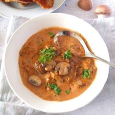 two bowls of soup with mushrooms and bread on the side