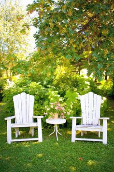 two white chairs sitting on top of a lush green field