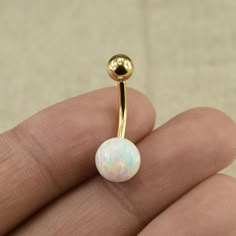 a gold nose ring with a white opal in the middle and a ball at the end