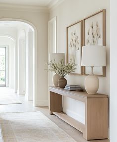 two vases with flowers sit on a table in front of a hallway leading to an open door