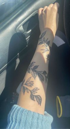 a woman's arm with leaves on it in the passenger seat of a car