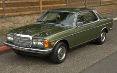 a green mercedes benz parked on the side of the road in front of a wooden fence