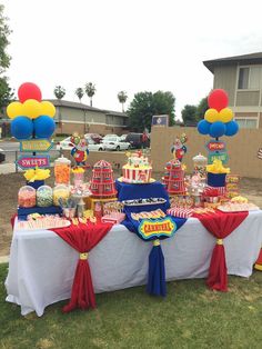 a table topped with lots of candy and balloons on top of a grass covered field