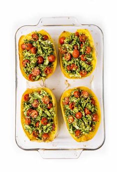 four stuffed yellow peppers with tomatoes and pesto on them in a baking pan, ready to go into the oven