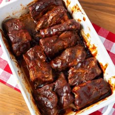 a white casserole dish filled with meat on a red and white checkered tablecloth