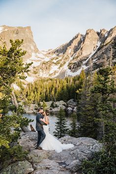 a bride and groom standing on rocks in the mountains