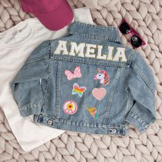 a denim jacket with embroidered patches on it and some sunglasses laying next to the jacket