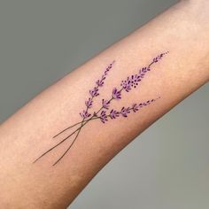 a purple flower tattoo on the left forearm and arm, with small flowers growing out of it