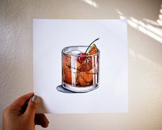 a hand holding up a drawing of a drink in a glass with an orange slice