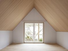 an empty room with a large window and wooden flooring on one side, looking out onto the trees outside