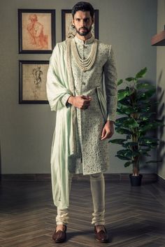 a man standing in a room wearing a white sherve and green shawl