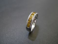 a yellow and white diamond ring sitting on top of a gray surface with two rows of diamonds in the middle