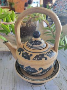 a tea pot with a wooden handle sitting on top of a plate next to a plant