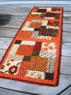 an orange and brown patchwork runner on a wooden deck