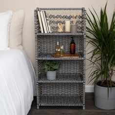 a wicker book shelf with books and plants on it next to a white bed