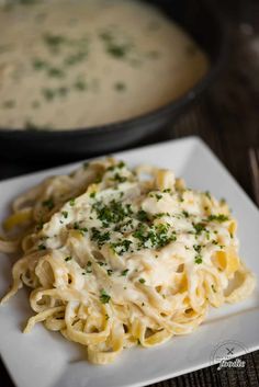 a white plate topped with pasta covered in sauce and parsley next to a skillet