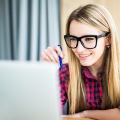 a young woman wearing glasses is looking at her computer screen and writing something on it