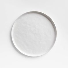 an empty white plate sitting on top of a white tableclothed surface with no one around it