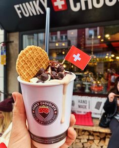 a person holding up a cup filled with ice cream and waffles in front of a store