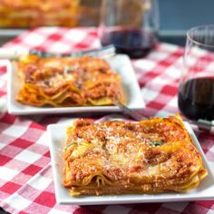 three square white plates with lasagna and cheese on red checkered tablecloth