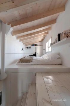 a bed sitting under a wooden ceiling in a room with white walls and wood flooring