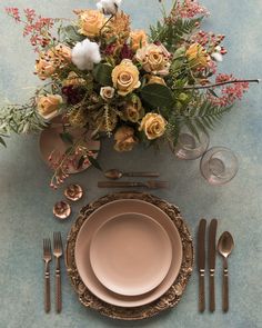 a table setting with pink and gold plates, silverware and flowers on the table